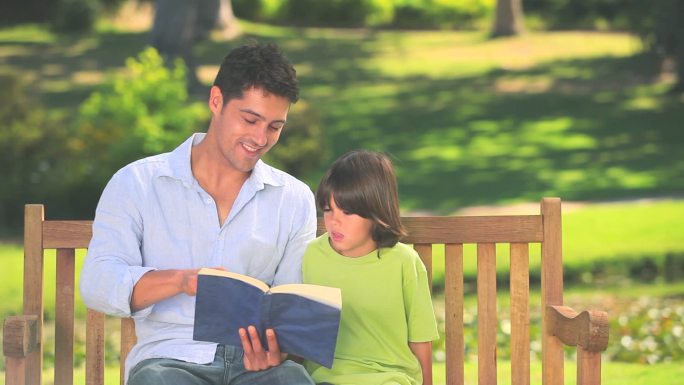 父亲和儿子坐在公园的长椅上看书