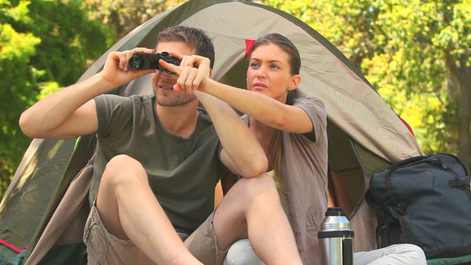 一对夫妇坐在帐篷外用望远镜看