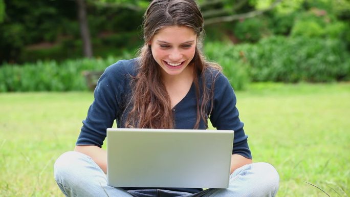 在公园里用笔记本电脑打字的快乐女人
