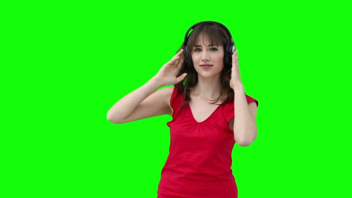 一个女人在绿色的背景下，拿着耳机对着她的头