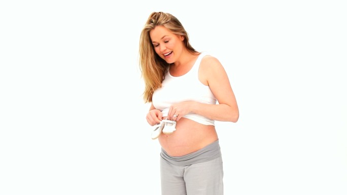 一个白人孕妇在玩婴儿鞋，在白色背景下