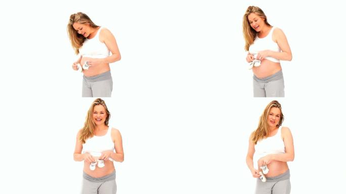 一个白人孕妇在玩婴儿鞋，在白色背景下