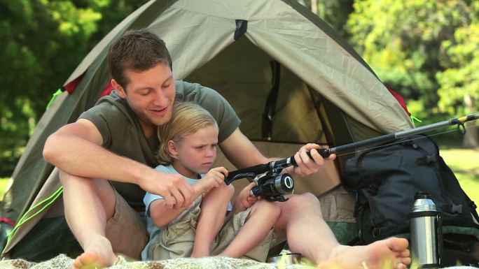 父亲在帐篷外教儿子如何使用鱼竿