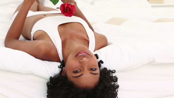 黑发女子手捧一朵红玫瑰放在床上