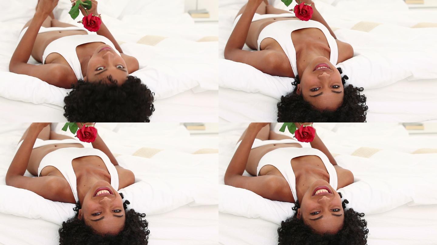 黑发女子手捧一朵红玫瑰放在床上