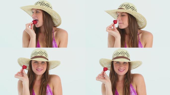 戴着沙滩帽的女人吃着白色背景下的草莓
