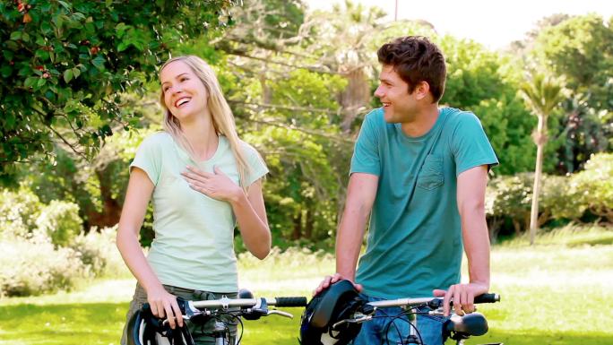 一对笑嘻嘻的情侣在公园里拿着自行车
