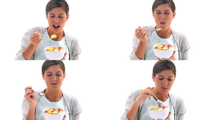 深色头发的女人吃着白色背景的水果沙拉