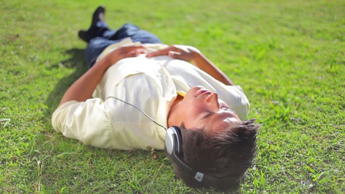 平静的黑发男子躺在草地上，在公园里听音乐