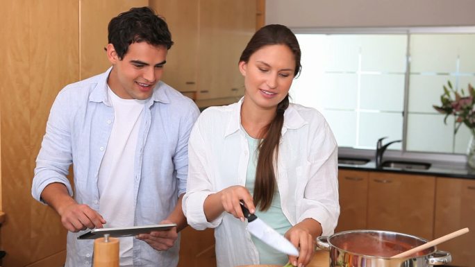 女人做饭，而丈夫用他的平板电脑指导