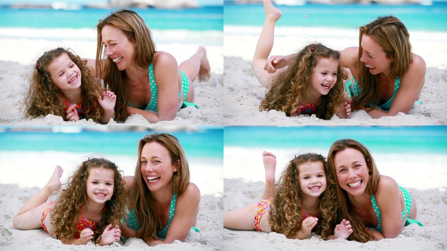 微笑的母亲在海滩上挠女儿痒痒