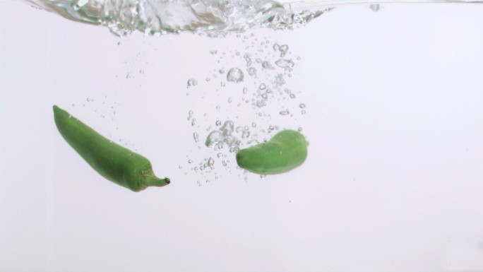 两个辣椒以超慢的动作在白色背景下落入水中