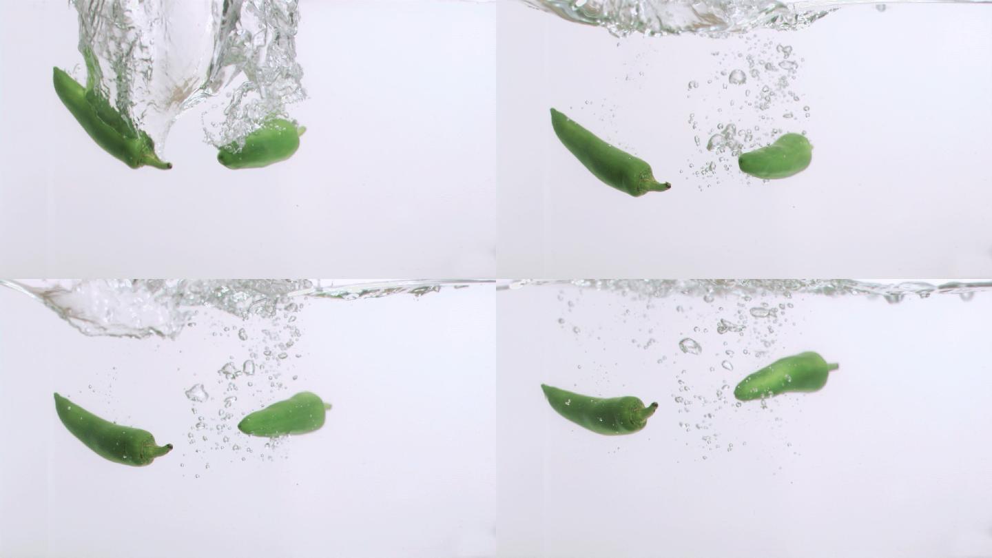 两个辣椒以超慢的动作在白色背景下落入水中