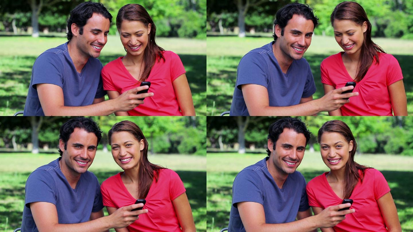 一对快乐的情侣在公园里看手机短信
