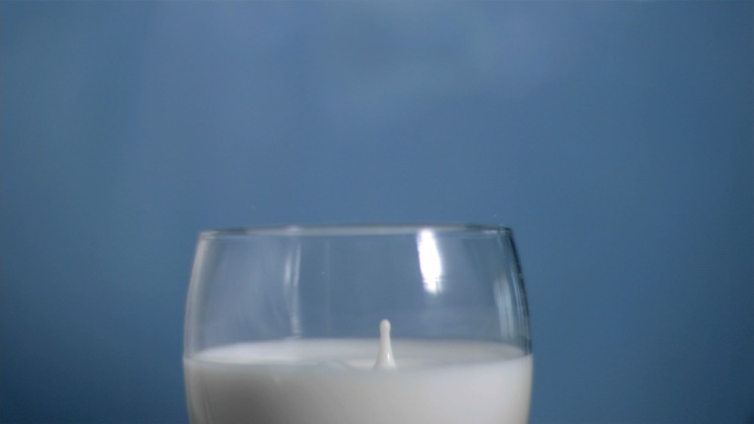 牛奶滴入玻璃杯慢镜头，在蓝色背景下