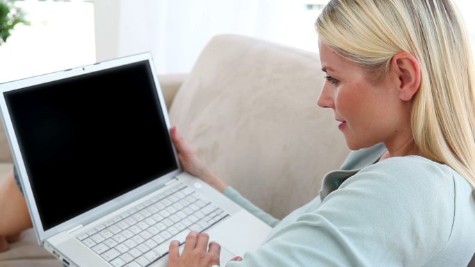 一个金发女人在沙发上用笔记本电脑