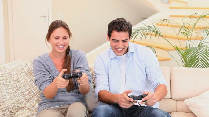 男人和女人坐在沙发上一起玩主机游戏，笑着