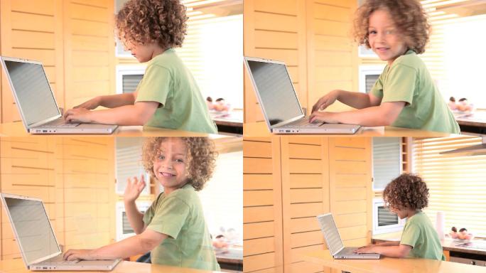 在厨房里，男孩一边在笔记本电脑上打字，一边对着摄像头挥挥手