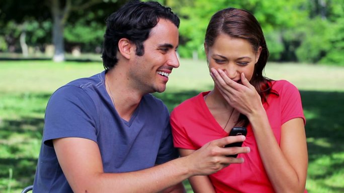 一对笑眯眯的情侣在公园里看手机短信