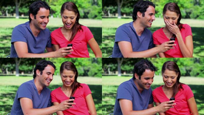 一对笑眯眯的情侣在公园里看手机短信