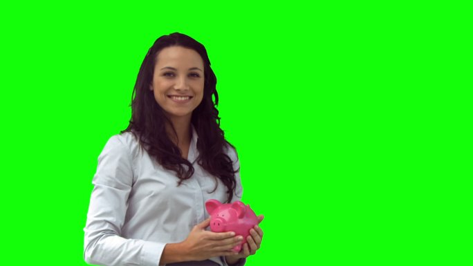 慢镜头里的女人拿着一个粉红色的储蓄罐，背景是绿色的