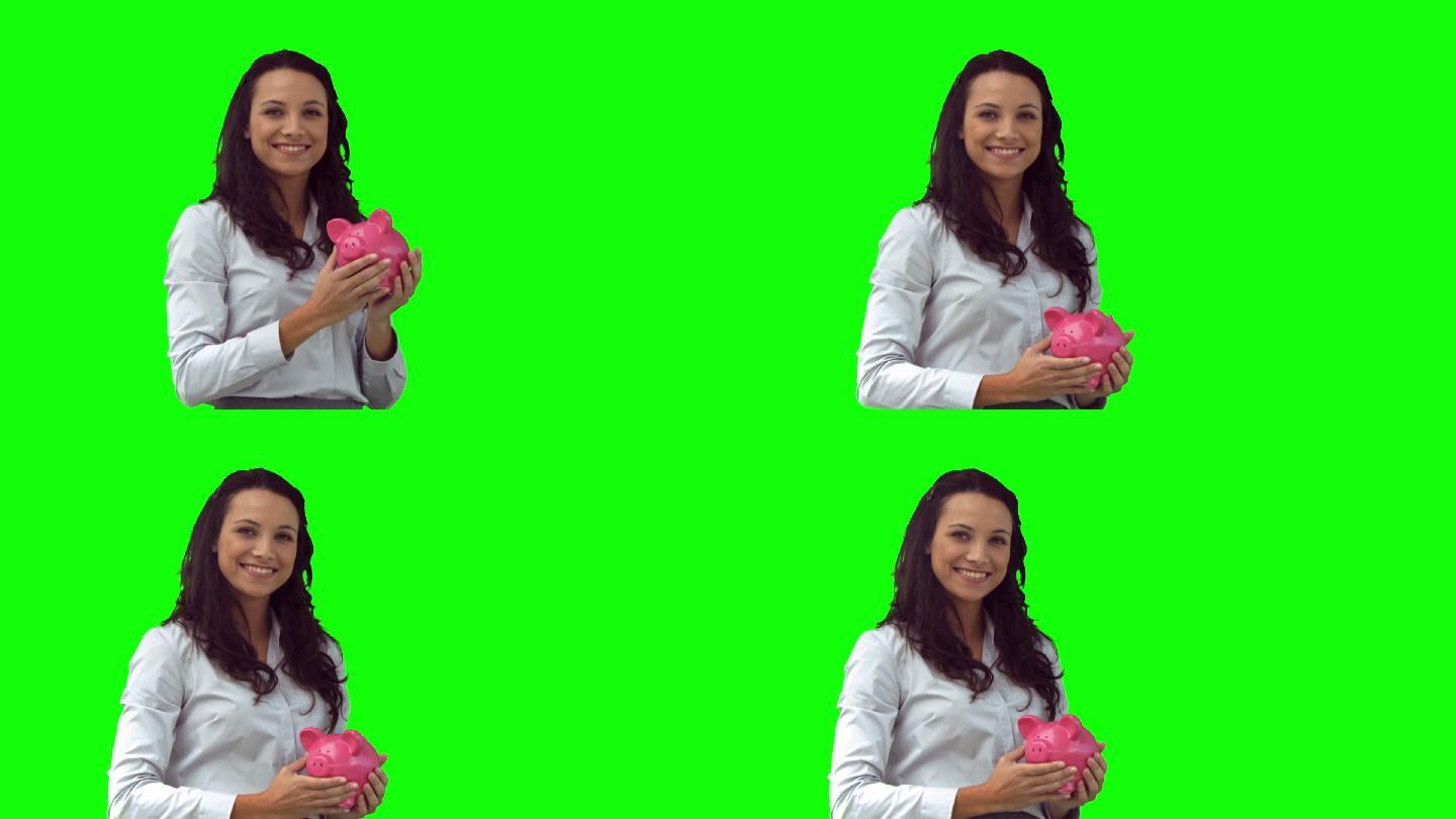 慢镜头里的女人拿着一个粉红色的储蓄罐，背景是绿色的