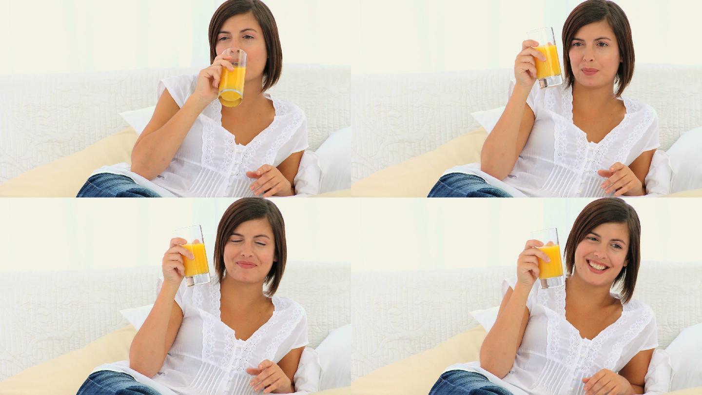 可爱的黑发女人坐在沙发上喝着橙汁