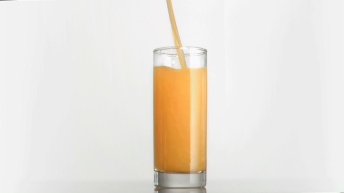 橙汁以超慢的动作流进白色背景的杯子里