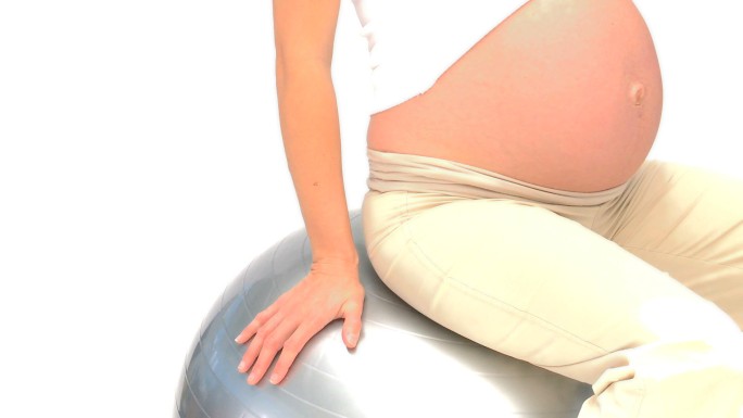 一名孕妇坐在健身球上，背景是白色