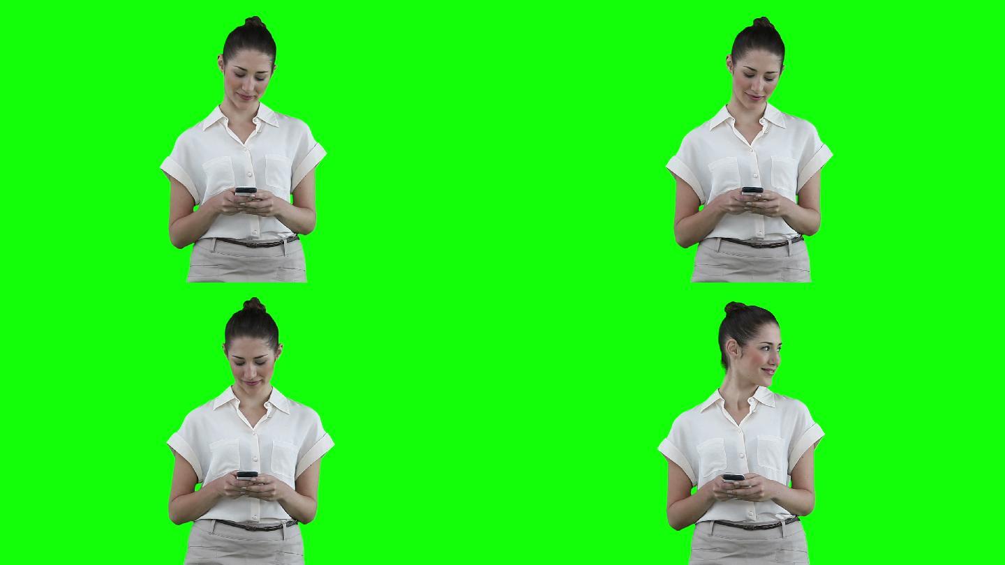 一名女子在用手机发短信，然后看向绿色背景下的身边