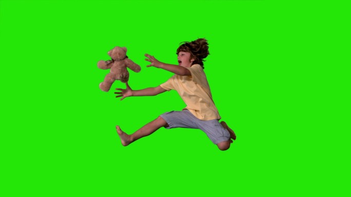 在慢镜头中，一个小男孩跳起来抓住绿色屏幕上的泰迪熊