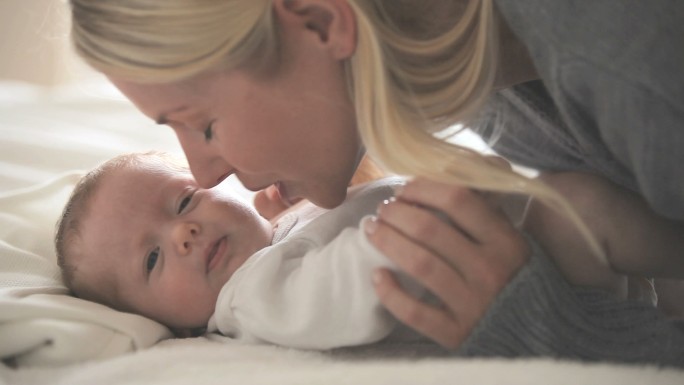 一位妇女抱着一个婴儿，他躺在白色的床上，向他的右侧看