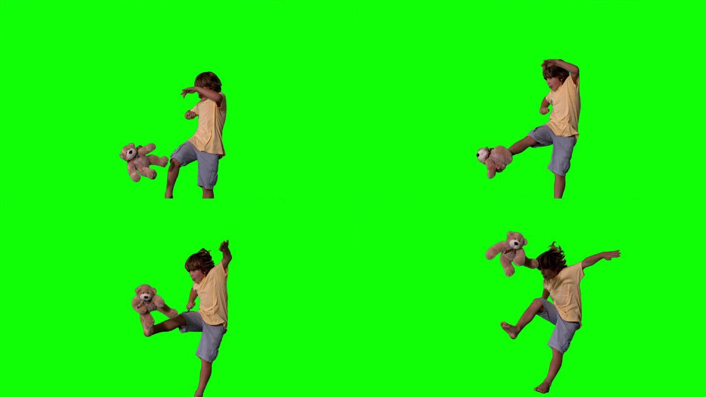 在慢动作的绿色屏幕上，小男孩跳起来踢泰迪熊