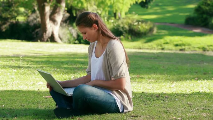 一个年轻女子坐在公园里用笔记本电脑