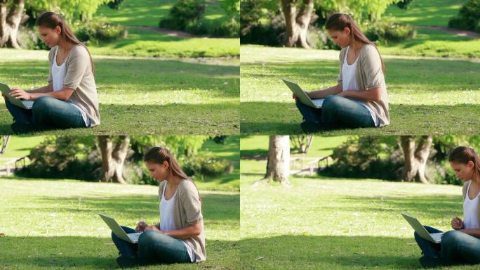 一个年轻女子坐在公园里用笔记本电脑