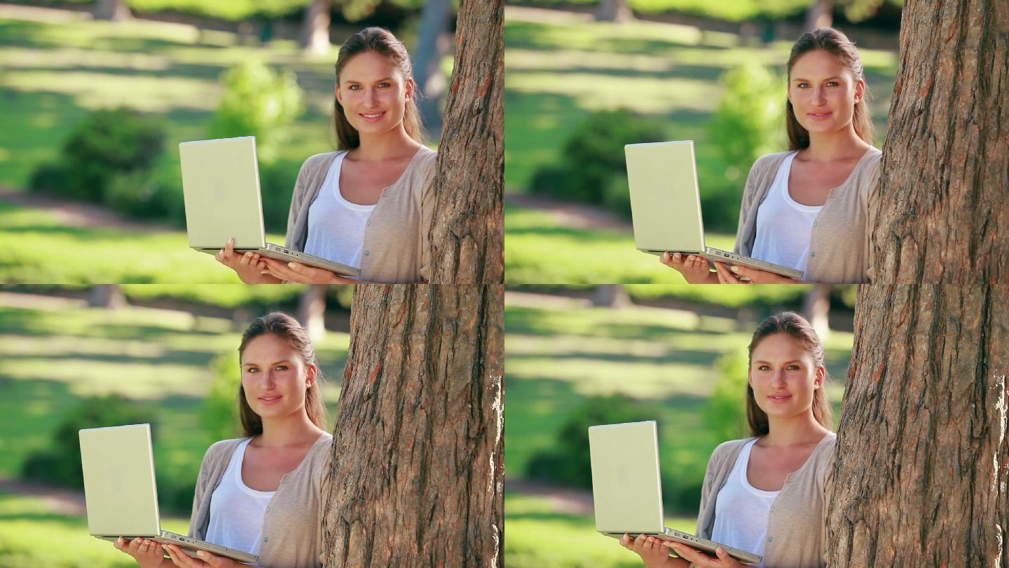 一位女士在公园里拿着一台笔记本电脑