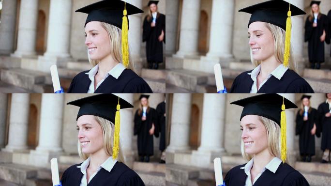 微笑的金发学生拿着她的文凭在大学前面