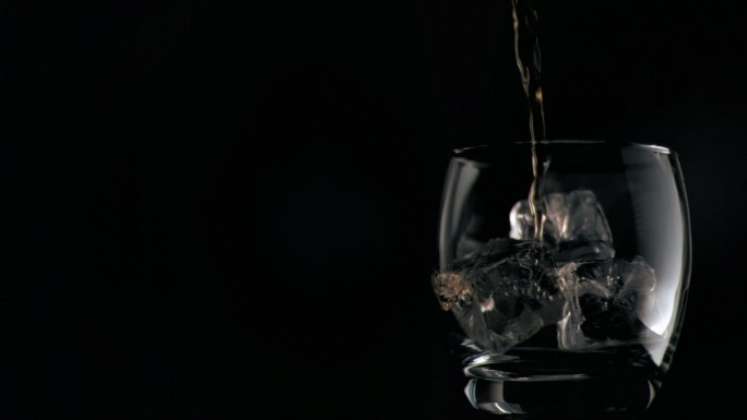 以超慢的动作将酒倒入装有冰块的黑色背景杯中