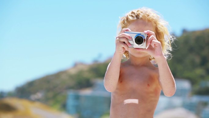 一个孩子在海滩上用数码相机拍照