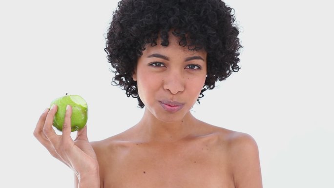 在白色背景下吃绿苹果的女人