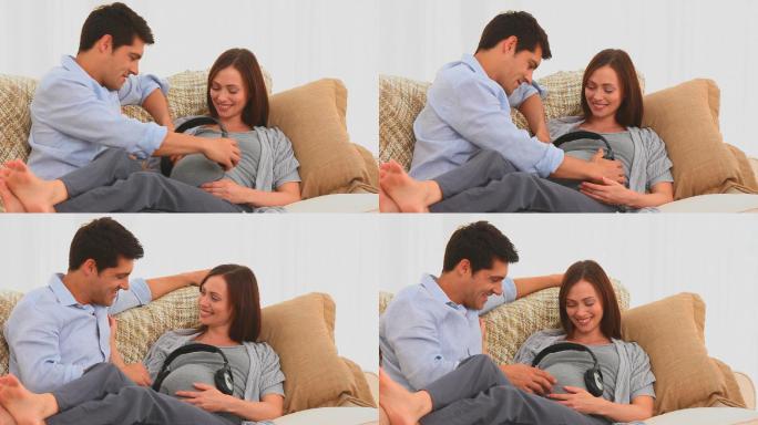一名男子在起居室里把耳机戴在他怀孕的妻子的肚子上