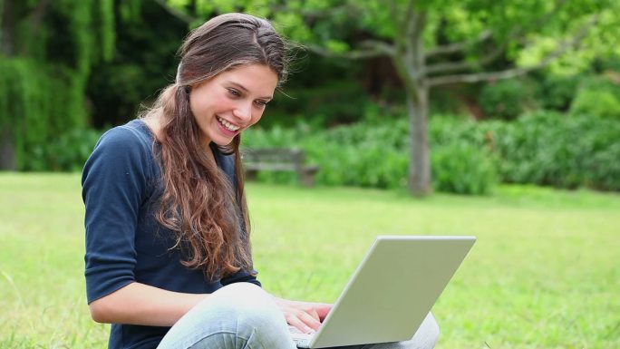 微笑的黑发女人在公园里用笔记本电脑