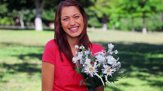 快乐的女人拿着鲜花在公园里笑