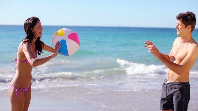 一对微笑的情侣在大海前玩沙滩球