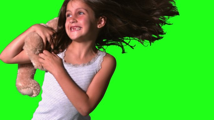 在慢镜头中，小女孩在绿色屏幕上旋转着抓住泰迪熊