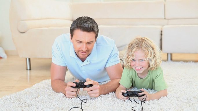 一对父子躺在地板上一起玩主机游戏