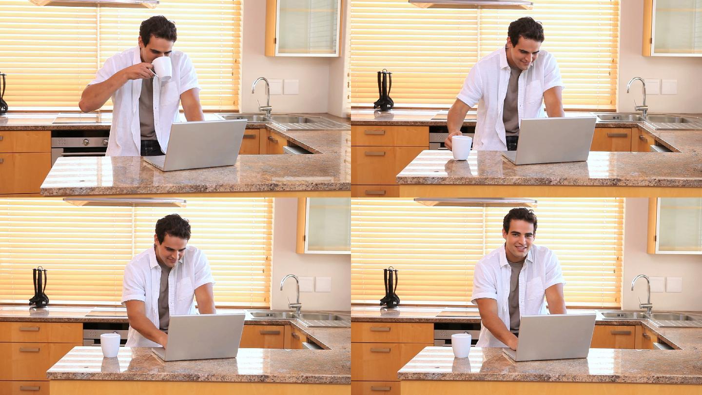一个男人在厨房边喝咖啡边用笔记本电脑