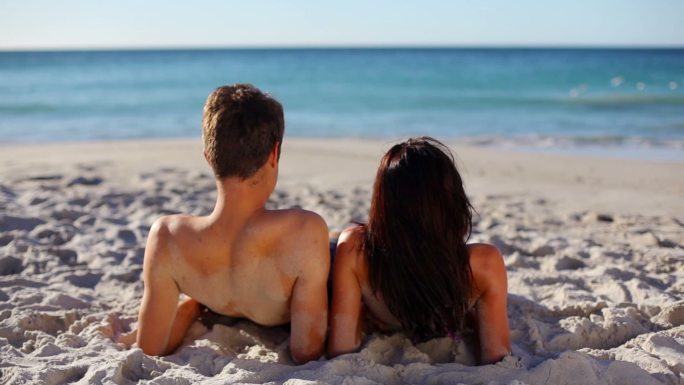 放松的夫妻躺在沙滩上的沙子上