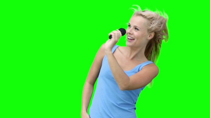 一个女人在绿色背景下对着麦克风跳舞唱歌