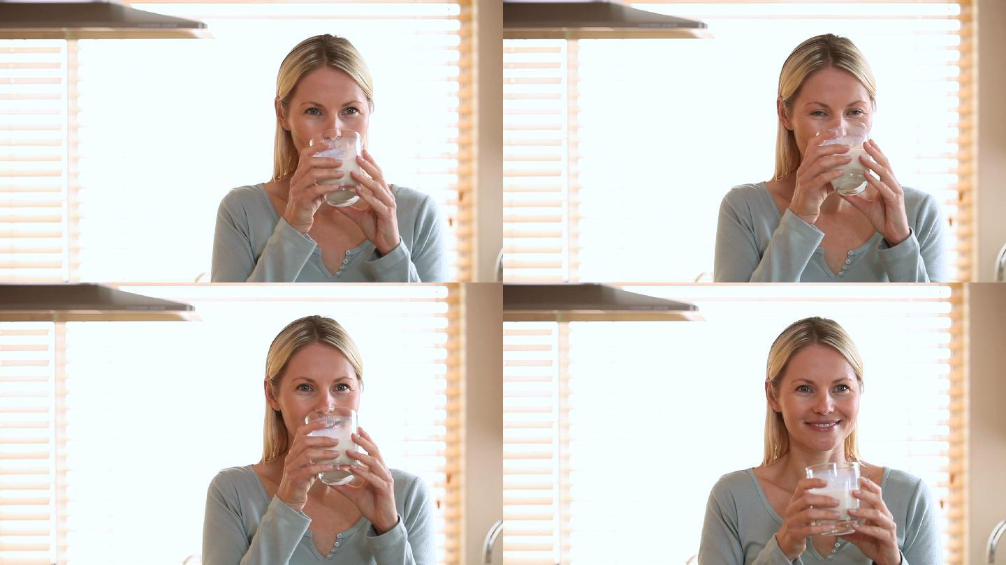 一个女人站在一个明亮的房间里，喝着她双手捧着的一杯牛奶